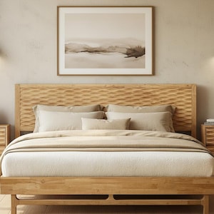 May include: A light wood bed frame with a carved headboard, layered with neutral-toned bedding. A framed landscape art piece hangs above the bed. Two matching nightstands flank the bed, each with a lamp and decorative items. The room has a warm, inviting aesthetic.