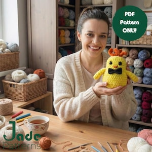 Może przedstawiać: Uśmiechnięta osoba trzyma żółtego szydełkowego kurczaka z czarną muszką i pomarańczowymi rogami. Obraz zawiera tekst "PDF Pattern ONLY" w zielonym okręgu i logo Jade Patterns. Widoczne są przędza i akcesoria do szydełkowania.