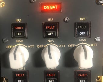 May include: A dark grey ADIRS 221 VU control panel featuring three white rotary knobs labelled OFF, NAV, and ATT. The panel includes illuminated indicators labelled ON BAT, IR1, IR2, IR3, ADR1, ADR2, and ADR3, with FAULT and OFF text displayed on buttons.