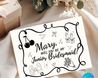 May include: A white card with black line art and the text "Mary, will you be my Junior Bridesmaid?" Cherries, hearts, champagne glasses, and a bouquet of flowers are also illustrated on the card. The card is on a white surface.