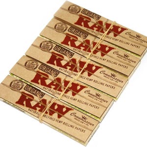 May include: A stack of six packs of RAW Organic Connoisseur King Size Slim rolling papers, held together with a rubber band. The packaging is tan with red text that reads "RAW Organic" and "Natural Unrefined Hemp Rolling Papers."