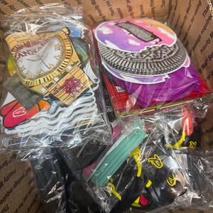 May include: A cardboard box filled with various stickers and accessories, including clock-themed designs, colorful circular stickers, and black accessories. The items are packaged in clear plastic bags, ready for shipping.
