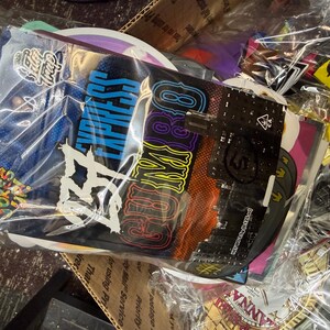 May include: A collection of colorful, sealed packages, likely for retail. The packages are in a clear plastic bag. The packages have various designs and text, including "EXPRESS" in blue and a logo. The overall theme is related to cannabis.