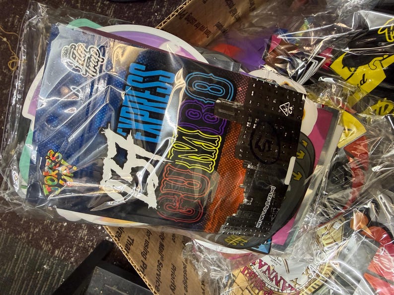 May include: A collection of colorful, sealed packages, likely for retail. The packages are in a clear plastic bag. The packages have various designs and text, including "EXPRESS" in blue and a logo. The overall theme is related to cannabis.