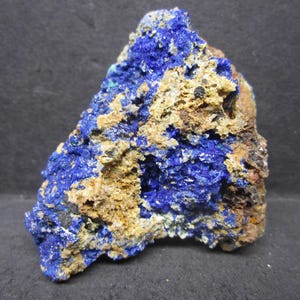 May include: A rough-hewn mineral specimen featuring a striking contrast of colors. Deep blue azurite crystals are interspersed with areas of tan and brown matrix, creating a visually interesting texture. The rock has a natural, unpolished appearance.