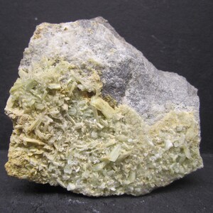 May include: A rough, irregularly shaped rock formation. The rock is primarily gray with patches of light green and yellow-brown crystalline structures. The crystals are clustered and appear to be small, needle-like formations.