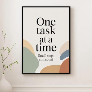 Peut inclure: Une affiche encadrée avec le texte "One task at a time" en gras noir. En dessous, le texte "Small steps still count" est en plus petit. Le fond est blanc cassé avec des formes abstraites aux couleurs sourdes. Un vase blanc avec de la verdure est à gauche.