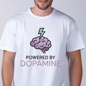 May include: White t-shirt featuring a purple brain graphic with a green lightning bolt and the text "POWERED BY DOPAMINE" in a purple font. The shirt is a crew neck style.