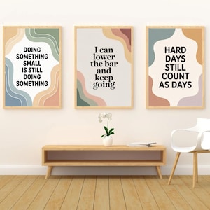 Peut inclure: Trois impressions d'art encadrées avec des citations inspirantes. Les impressions présentent une palette de couleurs neutres avec des formes abstraites dans des tons de bleu, vert, pêche et marron. Les citations se lisent : "FAIRE QUELQUE CHOSE DE PETIT, C'EST TOUJOURS FAIRE QUELQUE CHOSE".