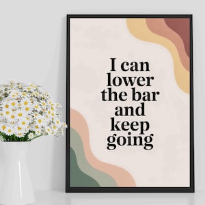 Op de afbeelding: Zwart omlijste kunstprint met de tekst "I can lower the bar and keep going". De achtergrond is lichtbeige met abstracte, golvende vormen in bruin, groen en perzik. Links staat een witte vaas met madeliefjes.