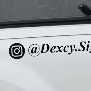 May include: A white vehicle with a black Instagram logo and the text "@Dexcy.Signs" on the side. The vehicle has a tinted rear window and a red taillight.