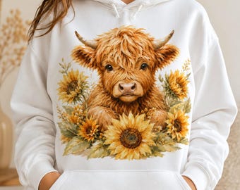 Pode incluir: Uma camisola com capuz branca com uma estampa gráfica de uma vaca Highland castanha e felpuda, rodeada por girassóis amarelos e folhas verdes. A peça tem mangas compridas, um bolso frontal tipo canguru e um capuz com cordões brancos.