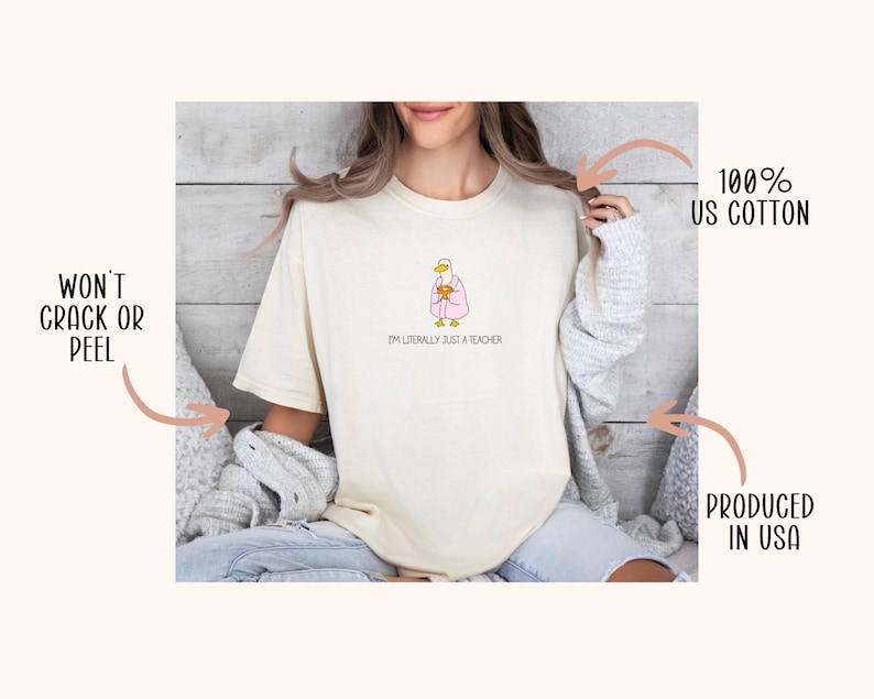 May include: Cream-colored t-shirt with a cartoon duck wearing a pink robe and holding a mug. The text "I'M LITERALLY JUST A TEACHER" is below the duck. The shirt is made of 100% US cotton.