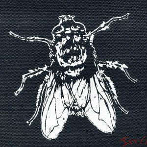 Puede incluir: Un parche de tela negro cuadrado con un gráfico serigrafiado en blanco de una mosca doméstica en el centro. La mosca se muestra con alas y patas detalladas. En la esquina inferior derecha, el texto rojo dice Irrlich Werkstatt en letra estilizada.