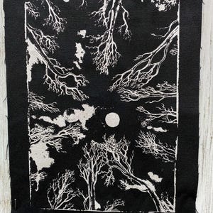 May include: A rectangular black fabric patch featuring a white screen-printed illustration of bare tree branches reaching toward a central full moon against a dark sky, with raw, unfinished edges and a visible rectangular border.