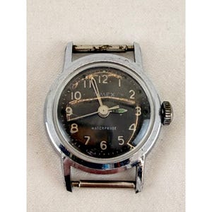 Könnte beinhalten: Eine Vintage-Timex-Armbanduhr mit schwarzem Zifferblatt und silberfarbenem Metallgehäuse. Die Uhr hat weiße Ziffern, Zeiger und das Wort "WATERPROOF". Eine klassische Uhr.