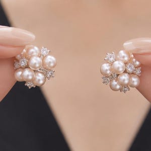 Peut inclure: Une paire de boucles d'oreilles en grappe composées de multiples perles rondes rose clair disposées en forme sphérique, entremêlées de petites pierres transparentes à facettes serties dans une monture métallique, créant un aspect floral texturé.