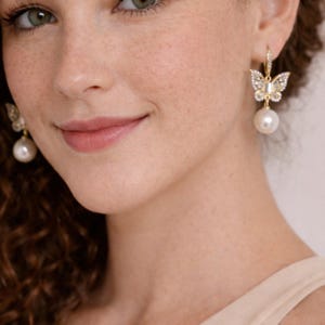 Pu&ograve; includere: Orecchini a farfalla color oro con cristalli trasparenti e una perla bianca pendente. Il design a farfalla presenta dettagli intricati e gli orecchini sono assicurati con una chiusura a leva. Un accessorio delicato ed elegante.
