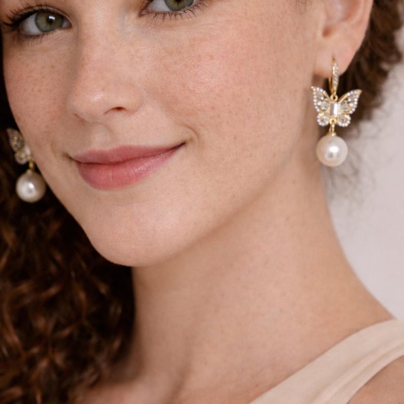 Pu&ograve; includere: Orecchini a farfalla color oro con cristalli trasparenti e una perla bianca pendente. Il design a farfalla presenta dettagli intricati e gli orecchini sono assicurati con una chiusura a leva. Un accessorio delicato ed elegante.