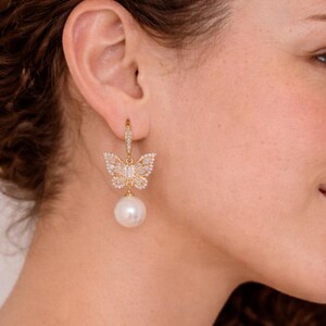 Pu&ograve; includere: Un orecchino a farfalla dorato con una perla pendente. Il design a farfalla &egrave; incastonato con piccoli cristalli trasparenti. L'orecchino &egrave; attaccato a un piccolo cerchio con cristalli aggiuntivi.