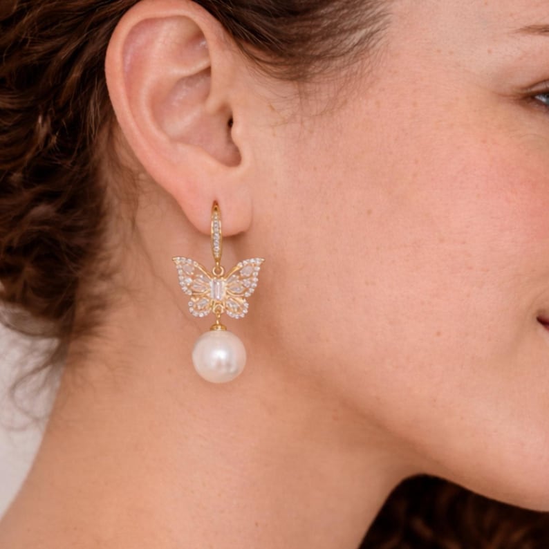 Pu&ograve; includere: Un orecchino a farfalla dorato con una perla pendente. Il design a farfalla &egrave; incastonato con piccoli cristalli trasparenti. L'orecchino &egrave; attaccato a un piccolo cerchio con cristalli aggiuntivi.