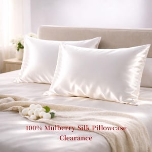May include: Two white silk pillowcases on a bed. The pillowcases are rectangular and have a smooth, shiny texture. The text "100% Mulberry Silk Pillowcase Clearance" is printed in red at the bottom of the image.