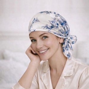 May include: A white silk head covering with a blue floral pattern. The head covering is tied at the back. The person in the image is wearing a cream-coloured satin shirt.