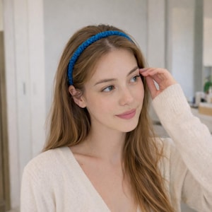 May include: A vibrant blue headband. The headband is made of a soft, textured material. The woman in the image is wearing a cream-colored sweater. The headband adds a pop of color to the look. The woman has long, light brown hair.