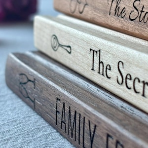 May include: A stack of three rectangular wooden blocks with engraved text and icons. The top block is light brown with a heart icon and the text The Sto. The middle block is pale wood with a spoon icon and the text The Secr. The bottom block is dark brown with two wine glasses and the text FAMILY, FRI.