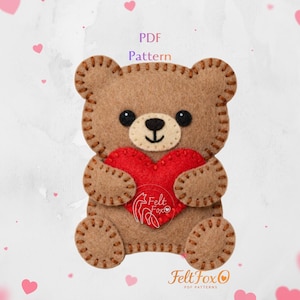 May include: A brown felt teddy bear holding a red heart. The bear has black eyes, a beige snout, and is stitched with brown thread. The image includes the text "PDF Pattern" and the Felt Fox logo.