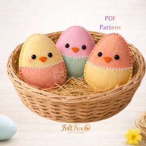 May include: Three colorful felt Easter egg decorations in a woven basket. Each egg is a different pastel color, with black eyes, orange beaks, and a beaded trim. The image includes the text "PDF Pattern" and the Felt Fox logo.