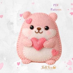 May include: A pink felt hamster holding a pink heart, with a white belly and accents. The hamster has black eyes and a brown nose. The image includes the text "PDF Pattern" and the Felt Fox logo.