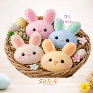 May include: A felt Easter basket filled with four bunny faces in pastel colors: pink, blue, yellow, and white. The bunnies have black eyes and pink noses. The basket also contains decorative eggs and flowers. The text "PDF Pattern" is visible.