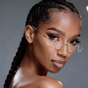 Puede incluir: Una mujer con piel oscura y cabello trenzado lleva gafas doradas en forma de onda adornadas con brillantes pedrería. Las gafas tienen un diseño decorativo único. El fondo es gris liso.