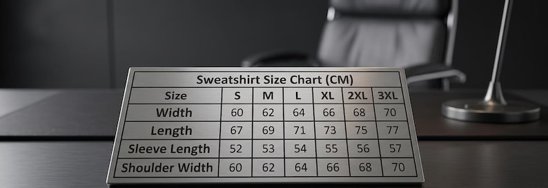 K&ouml;nnte beinhalten: Ein silbernes Metallschild mit einer Sweatshirt-Gr&ouml;&szlig;entabelle in Zentimetern. Die Tabelle enth&auml;lt die Gr&ouml;&szlig;en S bis 3XL mit Ma&szlig;en f&uuml;r Breite, L&auml;nge, &Auml;rmell&auml;nge und Schulterbreite. Das Schild liegt auf einer dunklen Oberfl&auml;che.