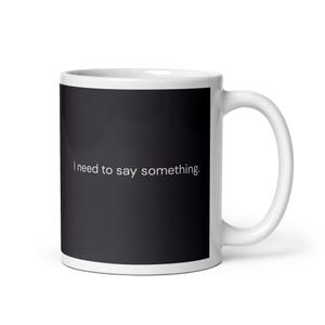 Könnte beinhalten: Weiße Keramik-Tasse mit schwarzem Hintergrund und dem Text "I need to say something." Die Tasse hat einen weißen Henkel und eine glänzende Oberfläche. Ein schlichtes, aber kühnes Design für den täglichen Gebrauch.