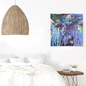 May include: A white bed with a white duvet cover and a white throw blanket. A woven basket sits at the foot of the bed. A woven pendant light hangs from the ceiling. A green plant in a woven basket sits on the floor. A painting of a blue and purple abstract floral design hangs on the wall. A small wooden side table with a glass top sits next to the bed.