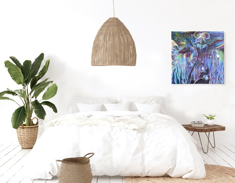 May include: A white bed with a white duvet cover and a white throw blanket. A woven basket sits at the foot of the bed. A woven pendant light hangs from the ceiling. A green plant in a woven basket sits on the floor. A painting of a blue and purple abstract floral design hangs on the wall. A small wooden side table with a glass top sits next to the bed.
