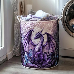 May include: A round laundry hamper with a purple dragon design. The dragon has large wings and is set against a moonlit background. The hamper is filled with folded blankets and towels and has white handles.