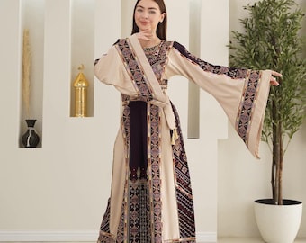 May include: A beige and burgundy embroidered dress with wide sleeves. The dress features intricate patterns along the sleeves, bodice, and hem. A matching sash cinches the waist. The dress is worn by a person.
