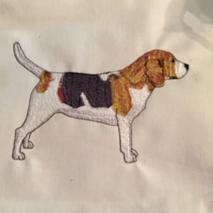 May include: Embroidered image of a beagle dog on a white fabric background. The dog is brown, black, and white with a long snout and floppy ears.