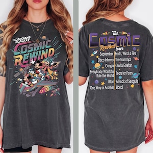 May include: Dark gray t-shirt featuring a colorful graphic of Disney characters on a spaceship with the text "COSMIC REWIND" and "GUARDIANS OF THE GALAXY". The back of the shirt has "The Cosmic Rewind Tour" text and a list of bands.