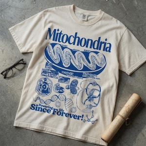 May include: A cream-colored short-sleeve t-shirt featuring a blue graphic print of a mitochondrion, DNA strands, and scientific diagrams. The text reads Mitochondria, we make ATP so you don't have to, no mitochondria no life, simple math, and Powering life Since Forever!