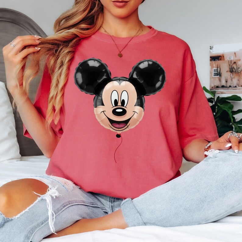 Puede incluir: Una camiseta roja con un dise&ntilde;o de globo de Mickey Mouse. El globo tiene orejas negras y una cara sonriente. La camiseta es de color liso y parece estar hecha de material suave.