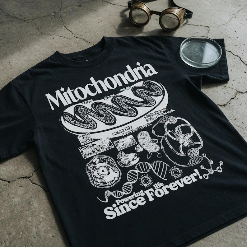 May include: A black t-shirt featuring a white graphic print of a mitochondrion, DNA strands, and cellular structures. The text reads Mitochondria, oxygen, glucose, energy, we make ATP so you don't have to, no mitochondria no life simple math, and Powering life Since Forever!