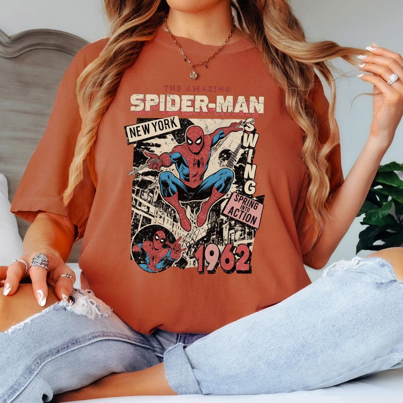 May include: Burnt orange t-shirt featuring a vintage Spider-Man graphic. The design includes the words "The Amazing Spider-Man," "New York," and "1962." The graphic shows Spider-Man in action, with a retro comic book style.