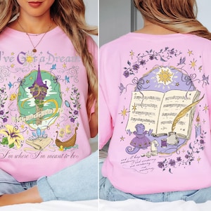 May include: Pink t-shirt with front and back graphics. The front features a tower, musical notes, and text that reads "I've Got a Dream" and "I'm where I'm meant to be." The back has an open book, sun, and text.