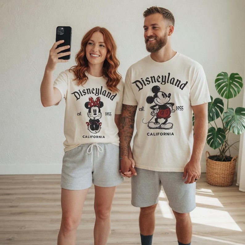 May include: Matching cream-colored Disneyland t-shirts with Mickey and Minnie Mouse graphics. The shirts have the text "Disneyland California 1955". The models are also wearing gray shorts.