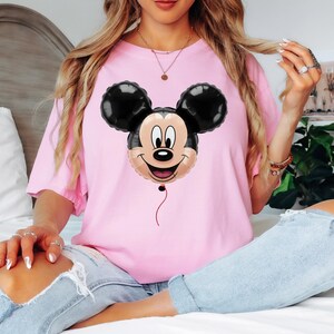 Puede incluir: Camiseta rosa claro con un dise&ntilde;o de globo de Mickey Mouse. El globo tiene orejas negras y una cara sonriente. La camiseta es de color liso y tiene mangas cortas.