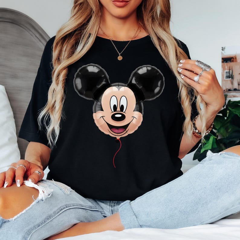 Puede incluir: Camiseta negra con un dise&ntilde;o de globo de Mickey Mouse. El globo tiene orejas negras, una cara beige y una cuerda roja. La camiseta es de estilo cuello redondo cl&aacute;sico.